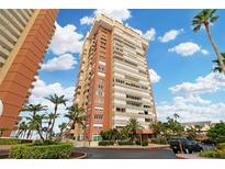 Exterior view of a tall, light-brown residential building with palm trees and a partly cloudy sky at 17920 Gulf Blvd # 205, Redington Shores, FL 33708