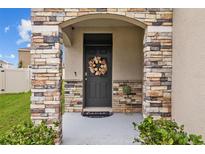Front entrance with stone pillars, a dark gray door, and fall decor at 17006 Wave Tressle Pl, Wimauma, FL 33598