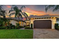 Elegant home with a large two-car garage, lush landscaping, and a vibrant sunset backdrop at 933 Riverscape St, Bradenton, FL 34208