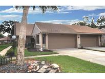 Tan colored two-unit condo building with a double garage and manicured lawn at 3230 Jademoor Cir, Palm Harbor, FL 34685