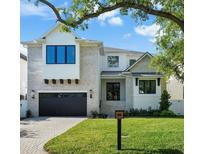 Beautiful two-story home with a manicured lawn, a brick driveway, and a black garage door underneath blue sky at 5024 W Dickens Ave, Tampa, FL 33629