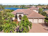 Stunning lakefront home with a red tile roof, three-car garage, and lush tropical landscaping at 7925 Royal Queensland Way, Lakewood Ranch, FL 34202