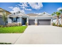 Two-story house with gray exterior, stone accents and three-car garage at 2251 Overfalls Pl, Wesley Chapel, FL 33543