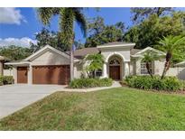 Tan house with brown garage doors, landscaping, and palm trees in the front yard at 711 Wildflower Dr, Palm Harbor, FL 34683