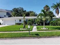 White single-story home with a spacious lawn, palm trees, and a two-car garage at 15301 Harbor Dr, Madeira Beach, FL 33708