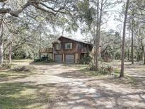 Rustic two-story home with wooden siding, a two-car garage, and nestled amongst mature trees at 1106 Oxbow Rd, Wimauma, FL 33598