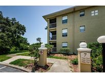 Multi-story tan condo building with balconies, surrounded by lush green landscaping and a clear blue sky at 2690 Coral Landings Blvd # 722, Palm Harbor, FL 34684