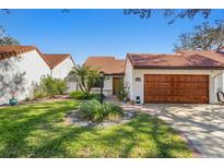 Front view of a charming villa with a landscaped lawn and wooden garage door at 11407 Robles Del Rio Pl, Temple Terrace, FL 33617