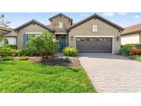 Charming home with a manicured lawn, stone accents, and a brick driveway leading to a two-car garage at 26810 Weiskopf Dr, Englewood, FL 34223