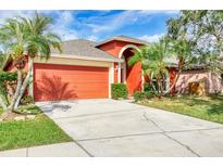 This single-story home features a bright red facade, a two-car garage, and mature landscaping at 27542 Sky Lake Circle, Wesley Chapel, FL 33544