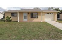 Tan home with attached garage and green lawn at 9816 Wayside Ln, Port Richey, FL 34668