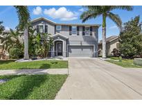 Two-story home with gray exterior, well-maintained lawn, tropical landscaping, and an attached two-car garage at 12013 Whistling Wind Dr, Riverview, FL 33579
