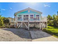 Elevated teal home with a wrap-around porch and a gravel driveway at 15823 Redington Dr, Redington Beach, FL 33708