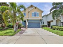 Two-story house with a light-yellow and blue exterior, two-car garage, and landscaped lawn at 6912 Makers Way, Apollo Beach, FL 33572