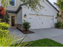 Home's white two-car garage with updated carriage doors, green lawn and landscaped beds at 8916 Arabella Ln, Seminole, FL 33777