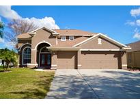 Two-story house with tan exterior, three-car garage, and manicured lawn at 2012 Fern Ridge Ct, Holiday, FL 34691