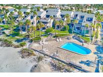 Aerial view of oceanfront condos surrounding a blue community pool and sundeck near sandy beach at 2100 Gulf Blvd # 13, Belleair Beach, FL 33786