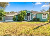 Green house exterior with attached garage and landscaped lawn at 9272 Eldridge Rd, Spring Hill, FL 34608