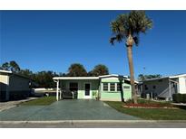 Quaint light green manufactured home with a covered patio and mature palm tree at 35127 Danny Dr, Zephyrhills, FL 33541