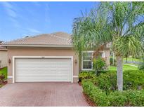 Tan house with white garage door, landscaping, and brick driveway at 5008 Cliff Bay Way, Wimauma, FL 33598