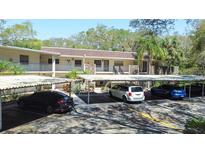 Low-rise condo building with covered parking and lush landscaping under a clear blue sky at 820 Patricia Ave # 207, Dunedin, FL 34698