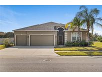 Tan three-car garage house with a landscaped lawn and palm trees at 13557 Bee Tree Ct, Hudson, FL 34669