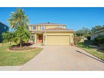 Two-story house with a yellow facade, paver driveway, and landscaping at 5709 White Trillium Loop, Land O Lakes, FL 34639