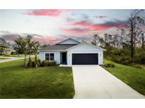 Single-story home with a light-colored exterior, dark garage door, and landscaping at 141 Hobo Rd, Rotonda West, FL 33947