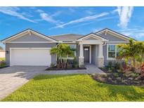 Beautiful gray house with stone accents, manicured lawn and garden, and a brick driveway on a sunny day at 11971 Starbright Path, Venice, FL 34293