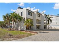 Charming condo with white stucco exterior, balconies, palm trees, and paved driveway at 9901 1St E St # F, Treasure Island, FL 33706