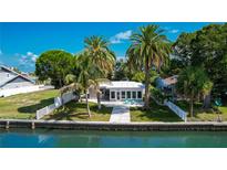 Charming waterfront home with lush tropical landscaping, white picket fence, and bright blue patio chairs at 341 Bahia Vista Dr, Indian Rocks Beach, FL 33785