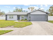 Front exterior of a single-story home with a gray facade, attached garage, and landscaped yard at 6090 114Th N Ter, Pinellas Park, FL 33782