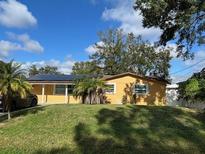 House exterior featuring a yellow single-story home with a solar panel system and a well-maintained lawn at 8823 W Robson St, Tampa, FL 33615