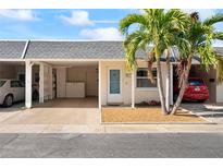 Front view of a condo with carport, landscaping, and palm trees at 224 Sky Loch E Dr, Dunedin, FL 34698
