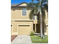 Two-story tan townhome featuring an attached garage, well-maintained lawn, and a mature palm tree at 5162 Bay Isle Cir, Clearwater, FL 33760