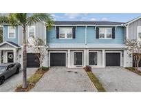 Three-unit townhome building with light blue siding, black garage doors, and a paved driveway at 2919 Grand Kemerton Pl, Tampa, FL 33618