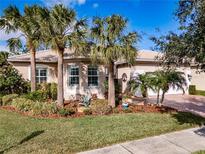 Tan house with palm trees, lush landscaping, and a two-car garage at 5006 Ruby Flats Dr, Wimauma, FL 33598