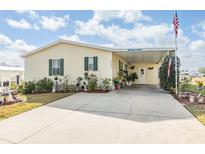 Single-wide yellow manufactured home with carport, landscaping, and American flag at 37340 Neukom Ave, Zephyrhills, FL 33541