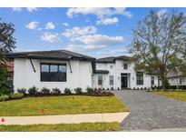 Stunning modern home featuring a white facade, dark trim, and a meticulously landscaped front yard and brick driveway at 10639 Ruffino Ct, Trinity, FL 34655