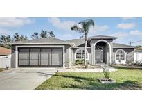 Gray house with a three-car garage and landscaped lawn at 5156 Mentmore Ave, Spring Hill, FL 34606