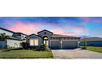 Charming one-story home featuring a two-car garage, paver driveway, well-maintained lawn, and colorful sunset sky at 9152 Warm Springs Cir, Parrish, FL 34219