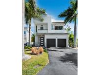 Modern two-story home featuring a clean white facade, black garage doors, and lush tropical landscaping at 2246 Fiesta Dr, Sarasota, FL 34231