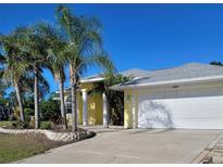 Charming yellow home featuring a spacious driveway and well-manicured lawn with palm trees, creating a welcoming curb appeal at 3447 Loveland Blvd, Port Charlotte, FL 33980