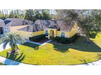 Charming one-story home boasts a lush lawn and vibrant yellow facade with mature landscaping at 5215 New Brittany Ln, Zephyrhills, FL 33541