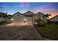 Beautiful exterior elevation with brick driveway, three-car garage, stone accents and professional landscaping at 19891 Bridgetown Loop, Venice, FL 34293