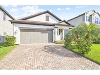 Charming home featuring a brick driveway, two-car garage, and tropical landscaping at 18015 Fenders Way, Land O Lakes, FL 34638