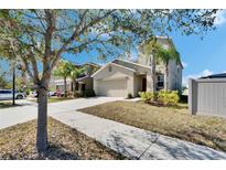 Tan two-story home with a two-car garage, palm trees, green shrubbery, and a concrete sidewalk at 6834 Blue Moon Way, Sun City Center, FL 33573