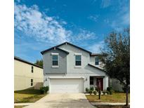 Two-story home with a two-car garage, red door, manicured lawn, and gray-blue exterior at 13456 Marble Sands Ct, Hudson, FL 34669