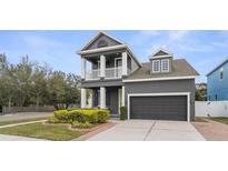 Two-story gray home featuring a second floor balcony and a well manicured lawn with yellow flowering bushes at 7602 S Desoto St, Tampa, FL 33616