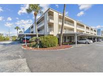 Condominium exterior with covered parking, mature landscaping, palm trees, and a beige facade against a blue sky at 215 Valencia Blvd # 106, Belleair Bluffs, FL 33770